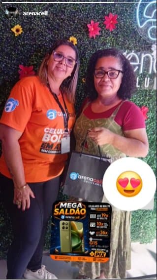 Cliente recebendo o celular novo na loja da Arena, ao lado da atendente